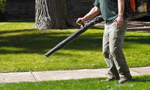 Crew member blowing grass clippings off a driveway after mowing in Houston
